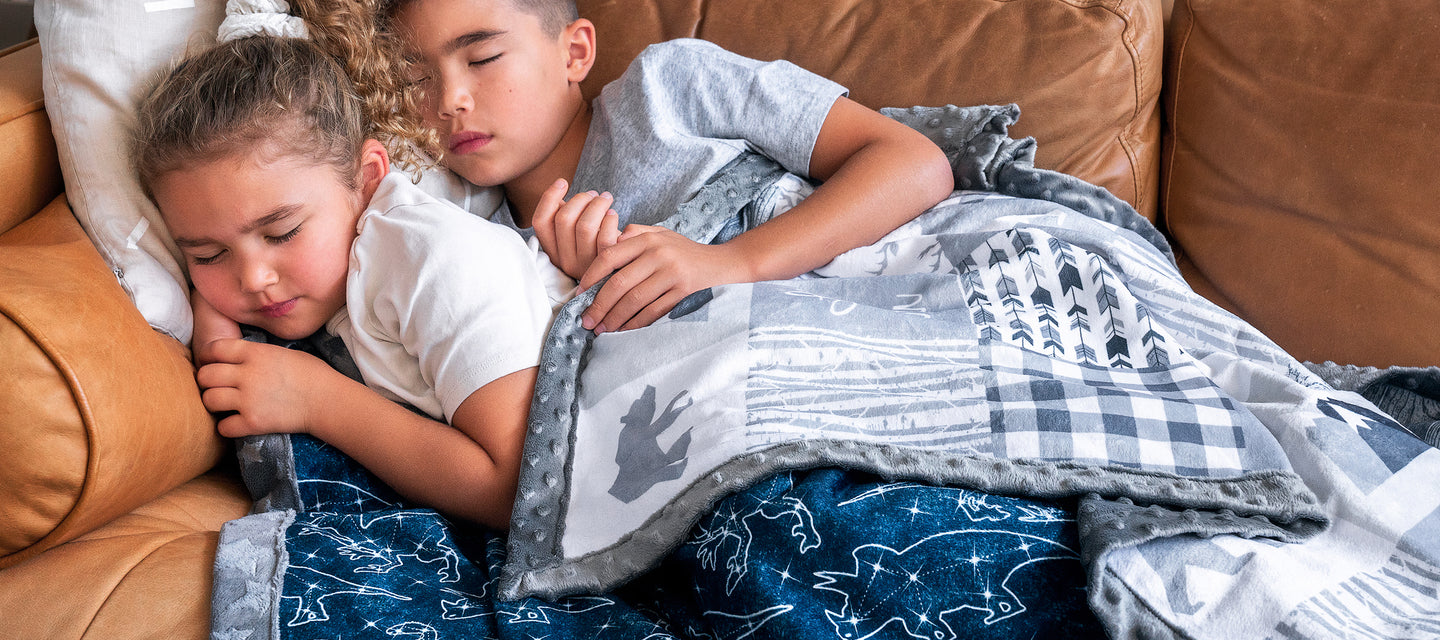 two children sleeping on the couch with a joomookie minky blanket draped over them woodland patchwork blanket with grey star minky fabric on the back
