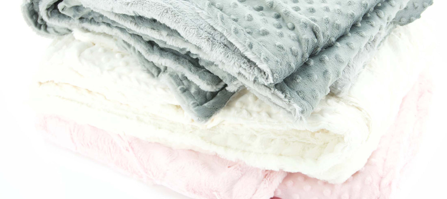 a pile of soft minky hide and dimple dot blankets in pink white and gray